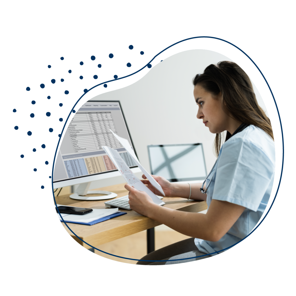 Büroarbeit in Arztpraxis: Frau sitzt am Computer und vergleicht zwei Papiere miteinander.