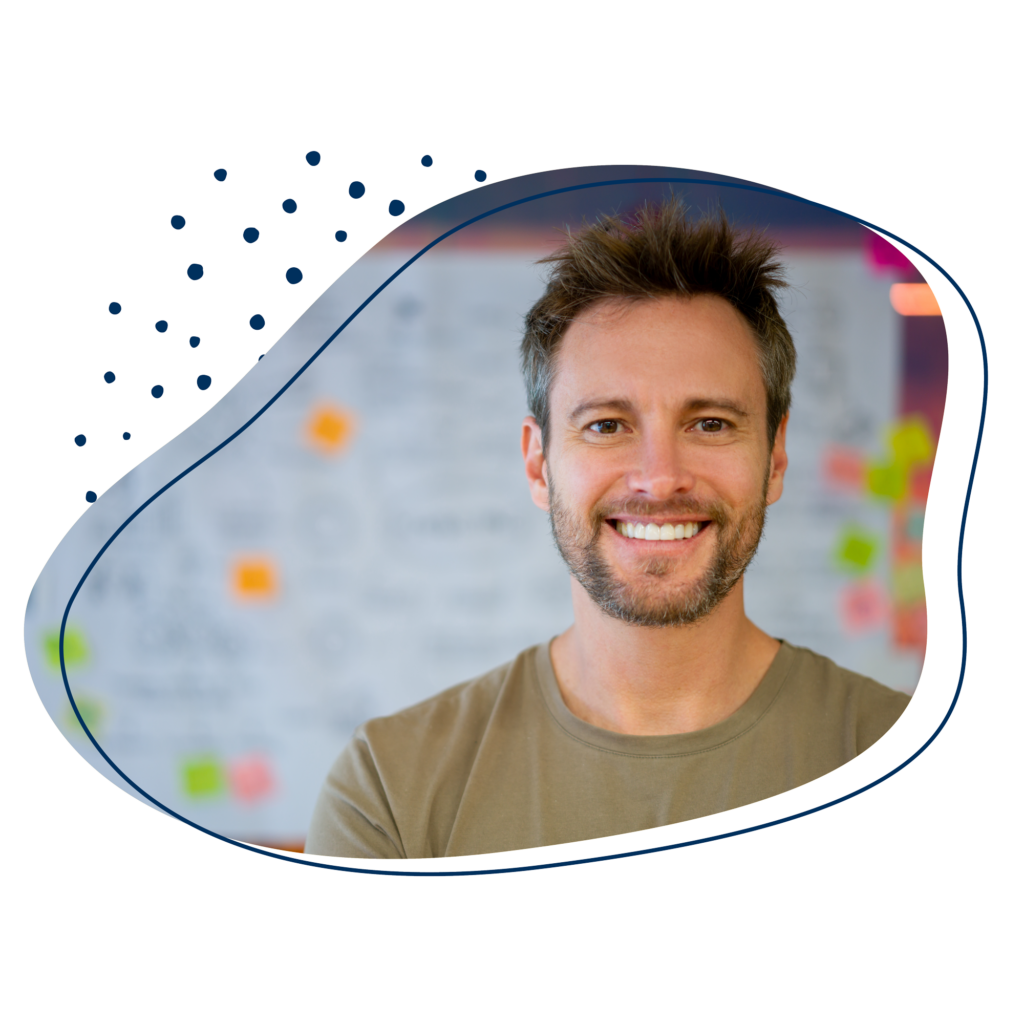 Mann lächelt in die Kamera, steht vor einer Pinnwand mit bunten Klebchen