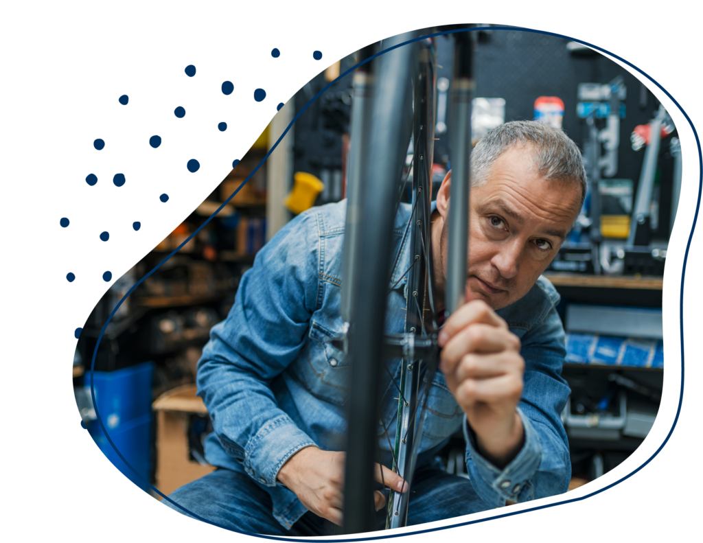 Ein älterer Mann mit grauen Haaren prüft in einer Fahrradwerkstatt das Rad eines Fahrrades.