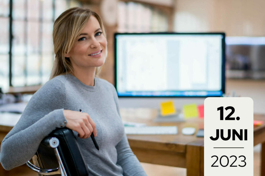 Frau sitzt an einem PC-Arbeitsplatz und dreht sich lächelnd zur Kamera